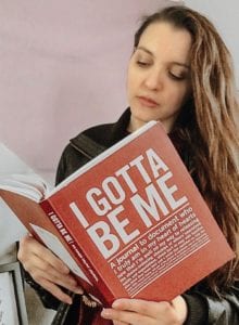 Photo of woman reading a book titled "I Gotta be Me- A journal to document who I truly am in my heart of hearts"