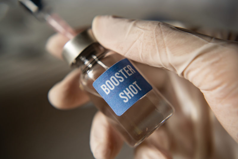 A medical professional holding a vial that reads "Booster Shot" on it.