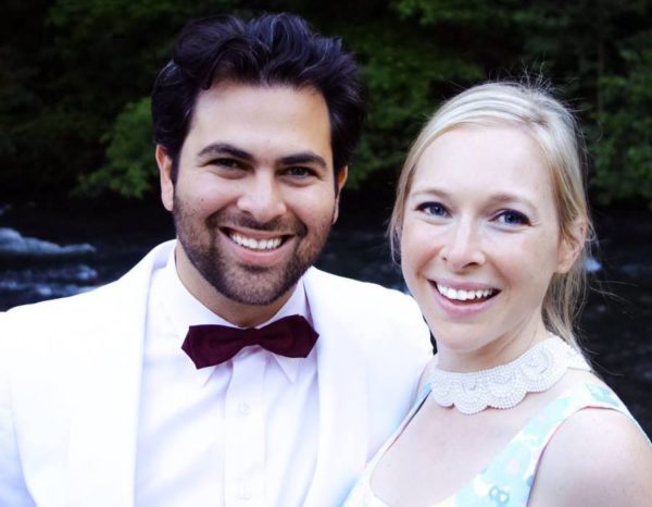 A photo of a man, Seth Ginsberg, wearing a white tuxedo and a woman, Cara Zelas wearing a printed dress.