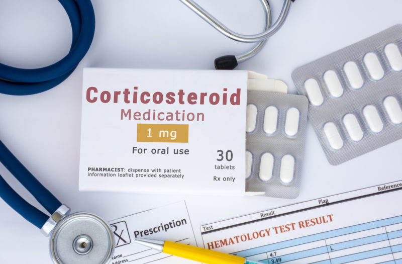 A corticosteroid medication or drug concept photo. On doctor table lies open packaging labeled "Corticosteroid medication" and fell out of blisters with pills treatment