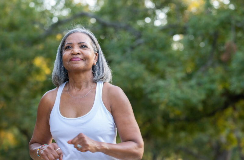 Photo of a Black senior citizen woman in a workout tank top going for a power walk in a park