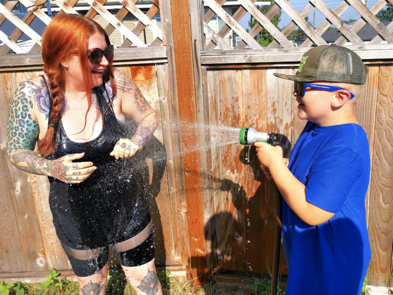 A photo of a woman being sprayed with a hose by a child.